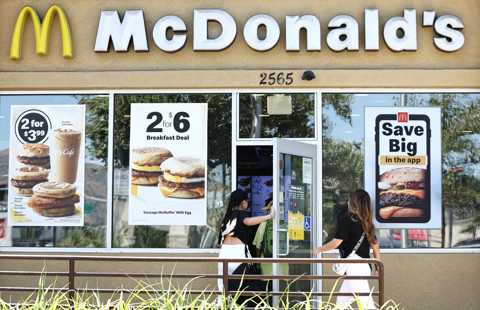 People enter a McDonald's restaurant that has posters on the windows advertising meal deals.