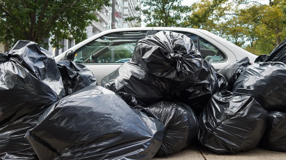 Black plastic trash bags in front of a parked car in city