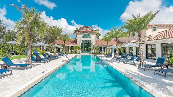 Pool surrounded by chairs and palm tress with a clubhouse at the end.