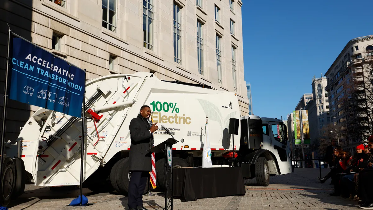 Man in jacket stands in front of electric white garbage truck