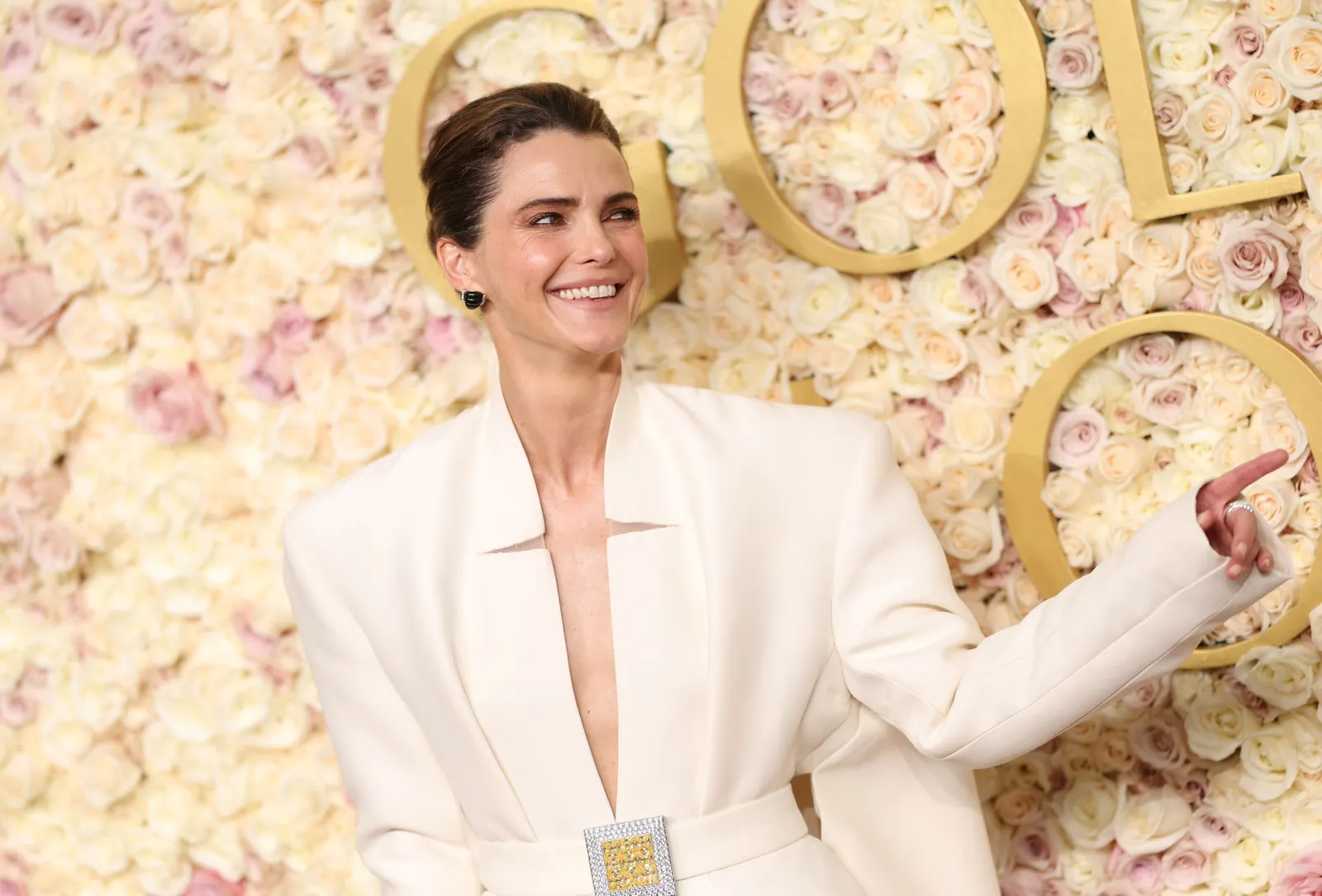 A person in a white big shouldered ensemble stands in front of a flowered wall.