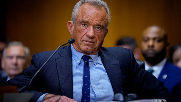 A person in a blue sit sits behind a desk at a hearing.