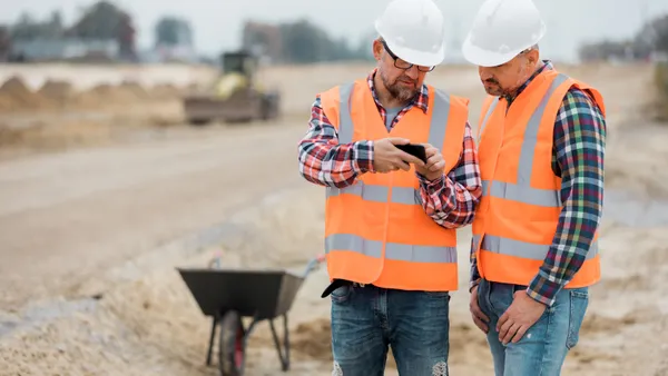 Two construction workers look at a phone