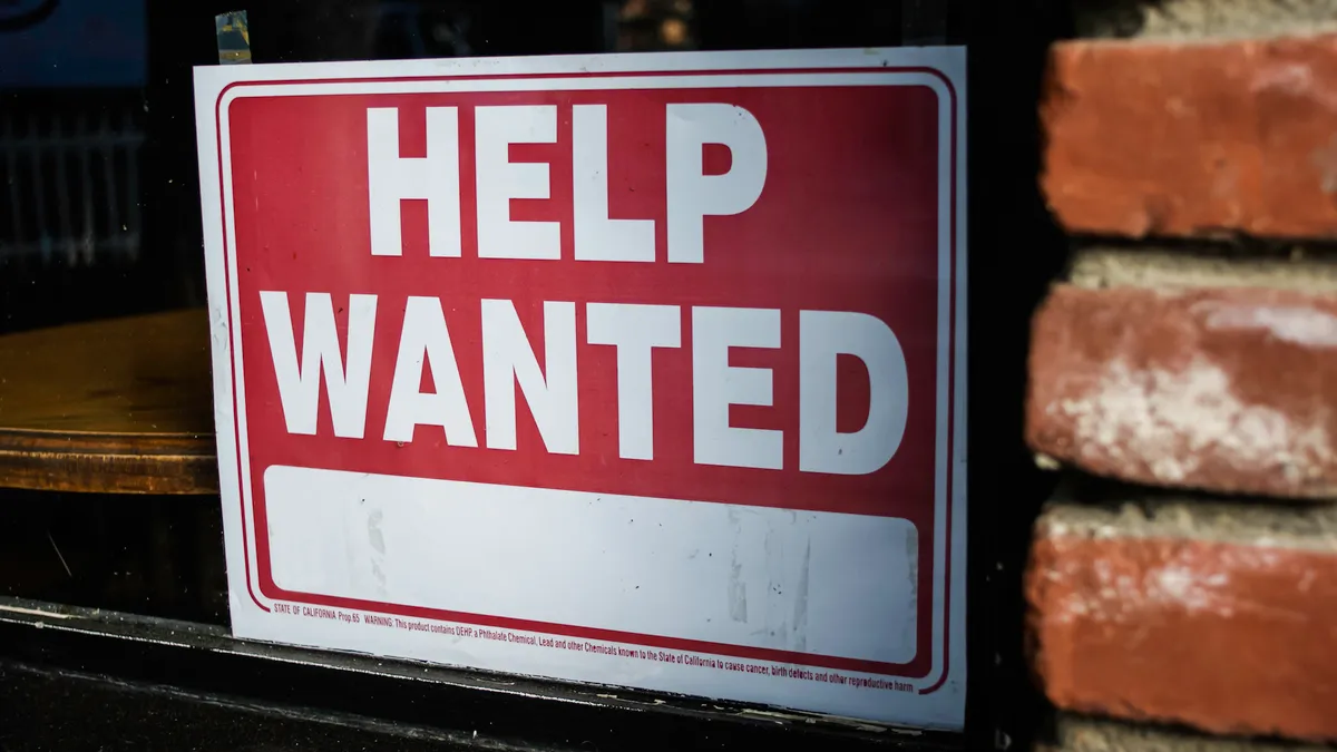 A 'Help Wanted' sign is displayed against a brick building