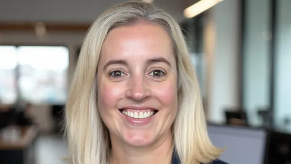 An image of a person smiling and wearing a blue blazer and white shirt