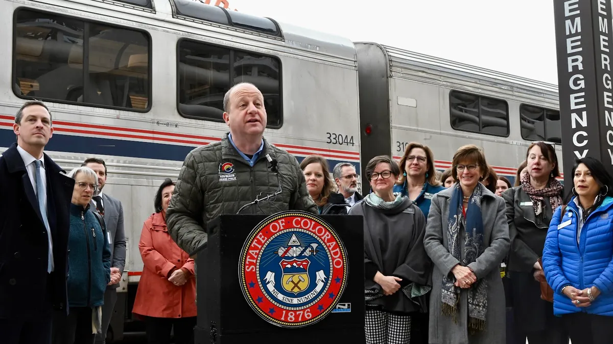 Man at podium with group of people and a train behind him.