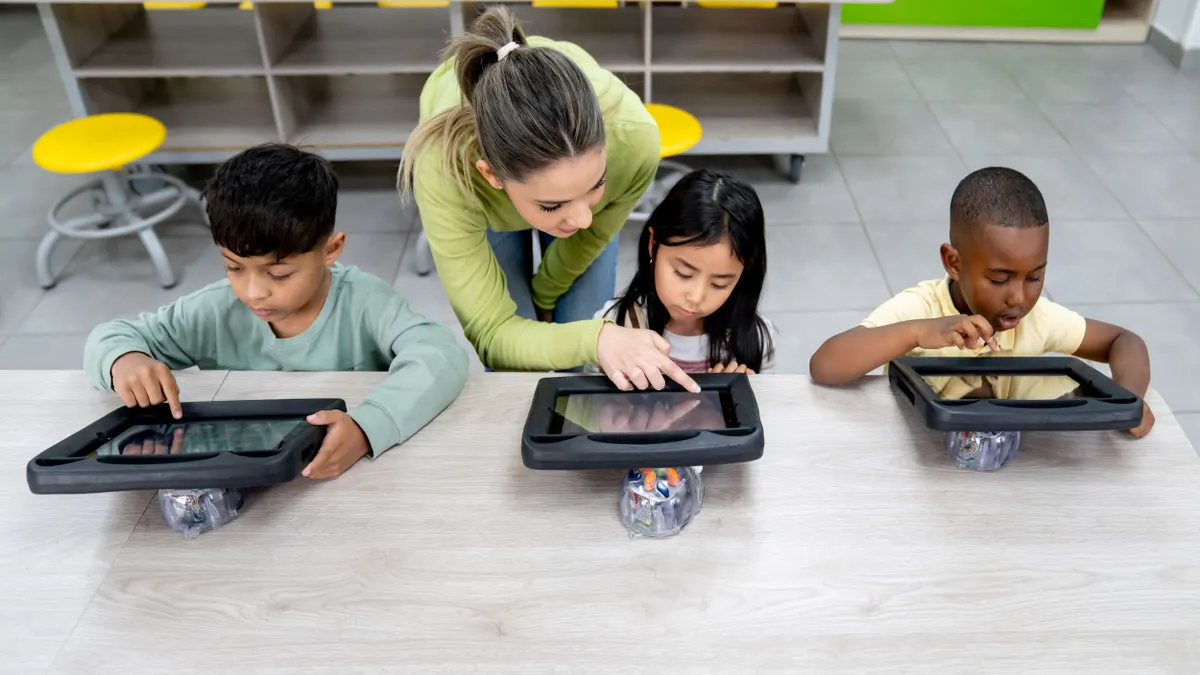 A teacher guides three young students using tablets in a classroom.