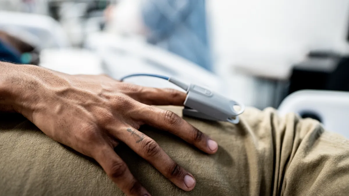 Close up of a person's hands with a pulse oximeter clipped on their pointer finger.