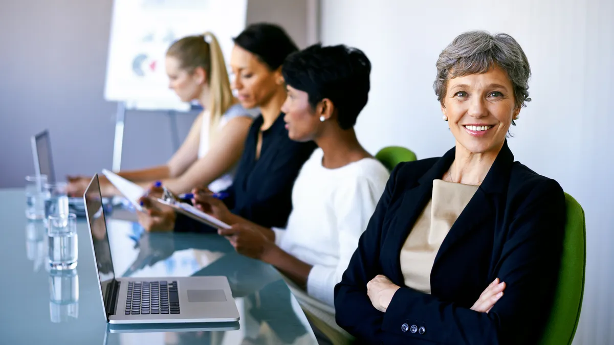 Woman smiling at camera, at workplace conference room table, other women in background