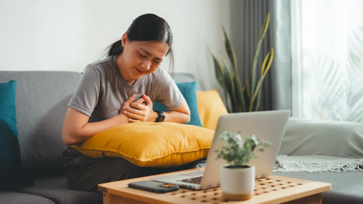 A picture of a woman suffering from chest pain sitting on sofa in living room at home.