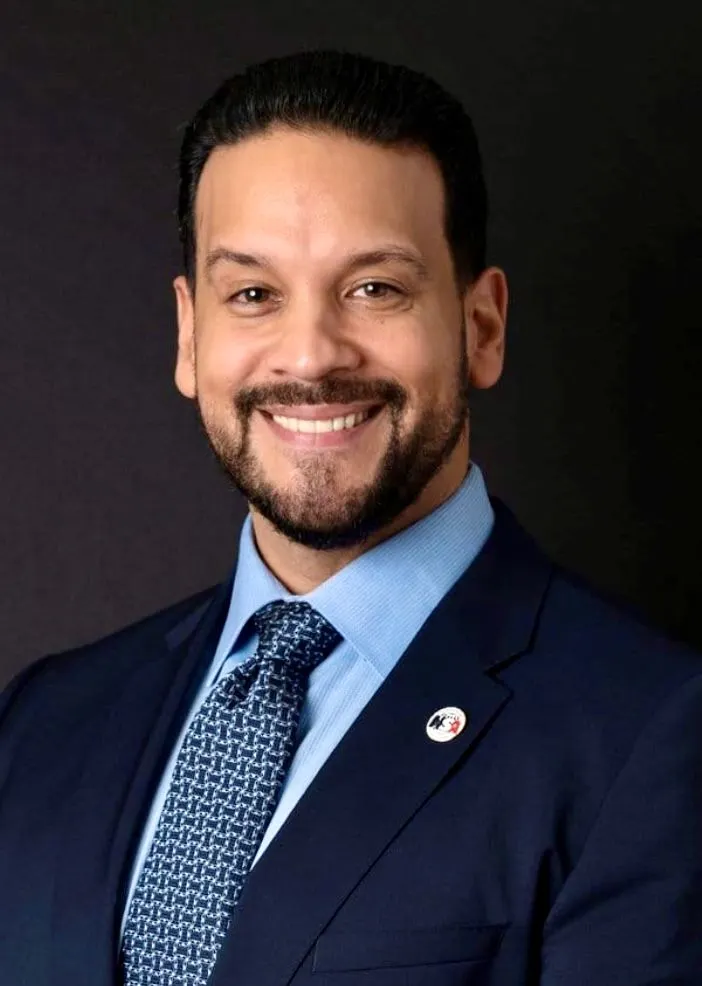 Headshot of a white, brunette man with some facial hair wearing in a suit and tie