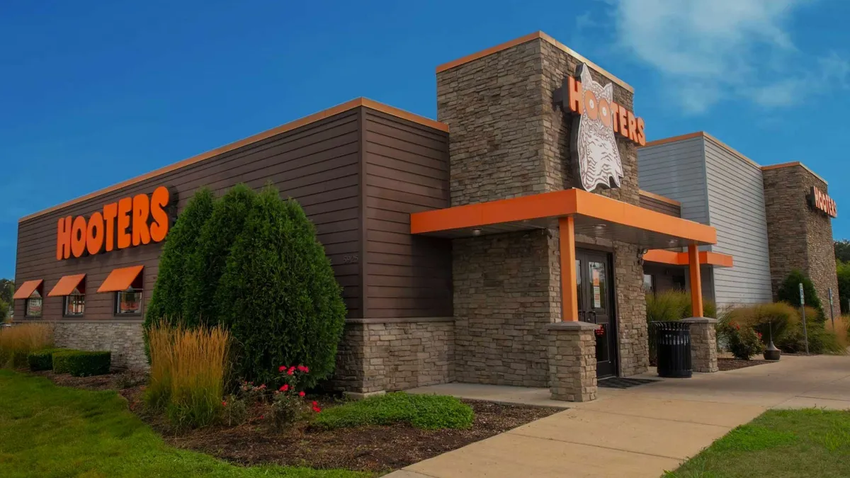 A photograph of a building with brown exteriors and orange trim with a Hooters sign that has an owl on an O.