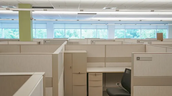 An office filled with cubicles and windows in the background.