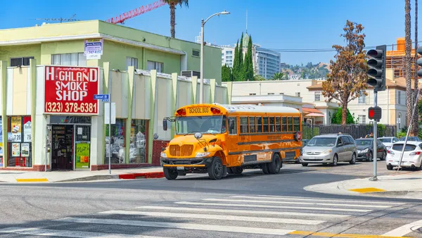A yellow school bus stands at an intersection with palm trees in the background