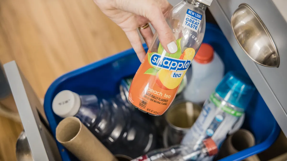 Empty plastic bottle of Snapple peach iced tea being placed into a recycling bin