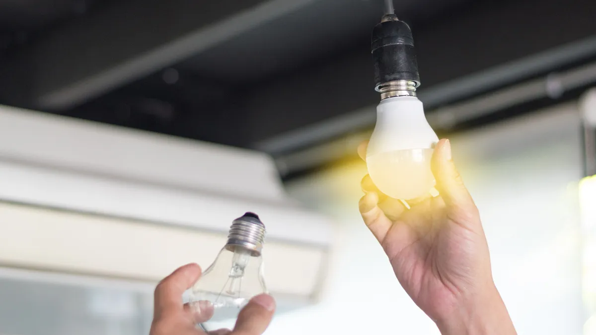 A closeup shot showing the hand of a man who is replacing a compact-fluorescent bulb with a new LED light fixture.