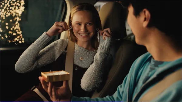 A person sitting in the front seat of a car holds up a pair of earrings