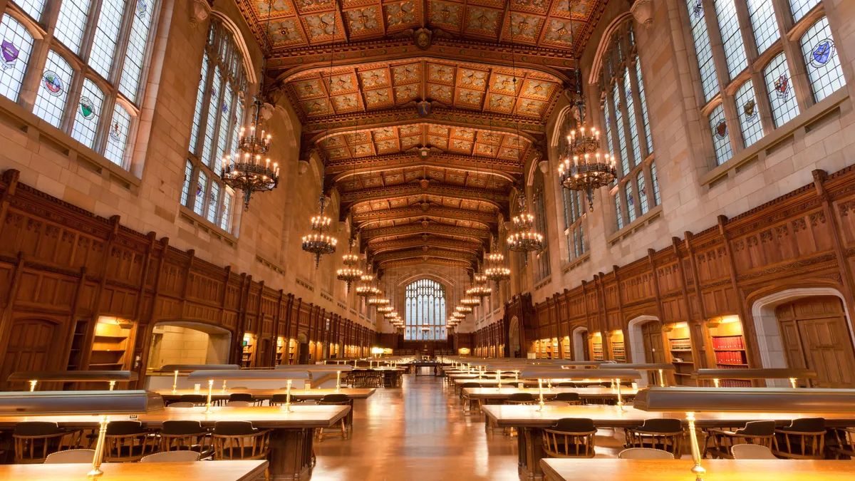 A long room with many tables, a high ceiling and chandeliers.