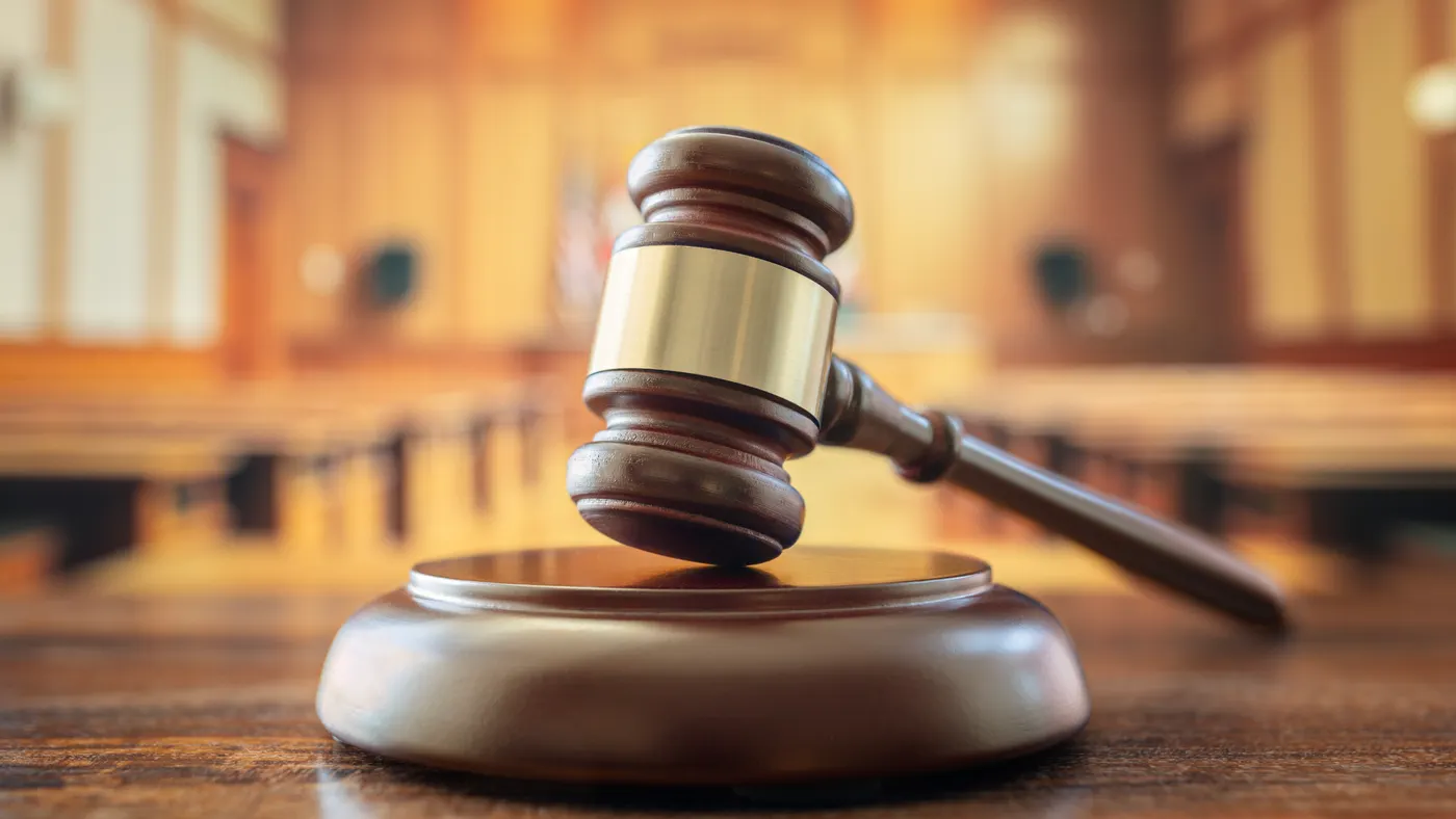A judge's gavel is shown in a close-up photo sitting on a pedestal on a desk in a courtoom