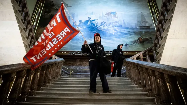Insurrectionist waving a "Trump is President" flag on the steps inside the Capitol building