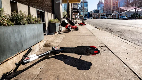 Several scooters lay on their sides along a sidewalk in an urban setting.