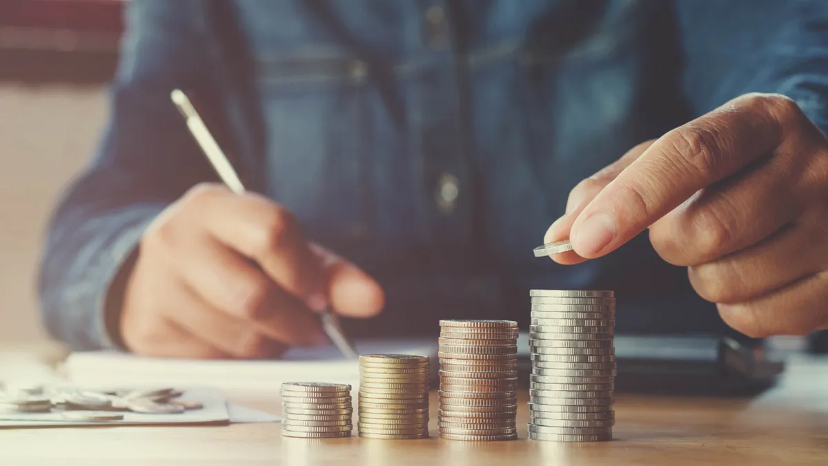 A person stacks coins on a table in an ascending order.