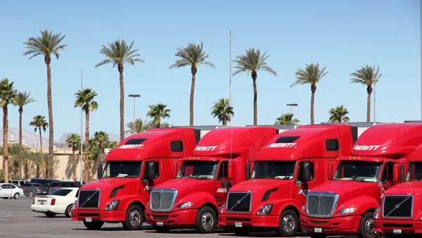 Red semitrucks parked in Las Vegas with palm trees in the background.