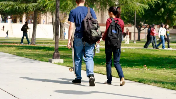 Two college students walk side by side down a campus sidewalk.
