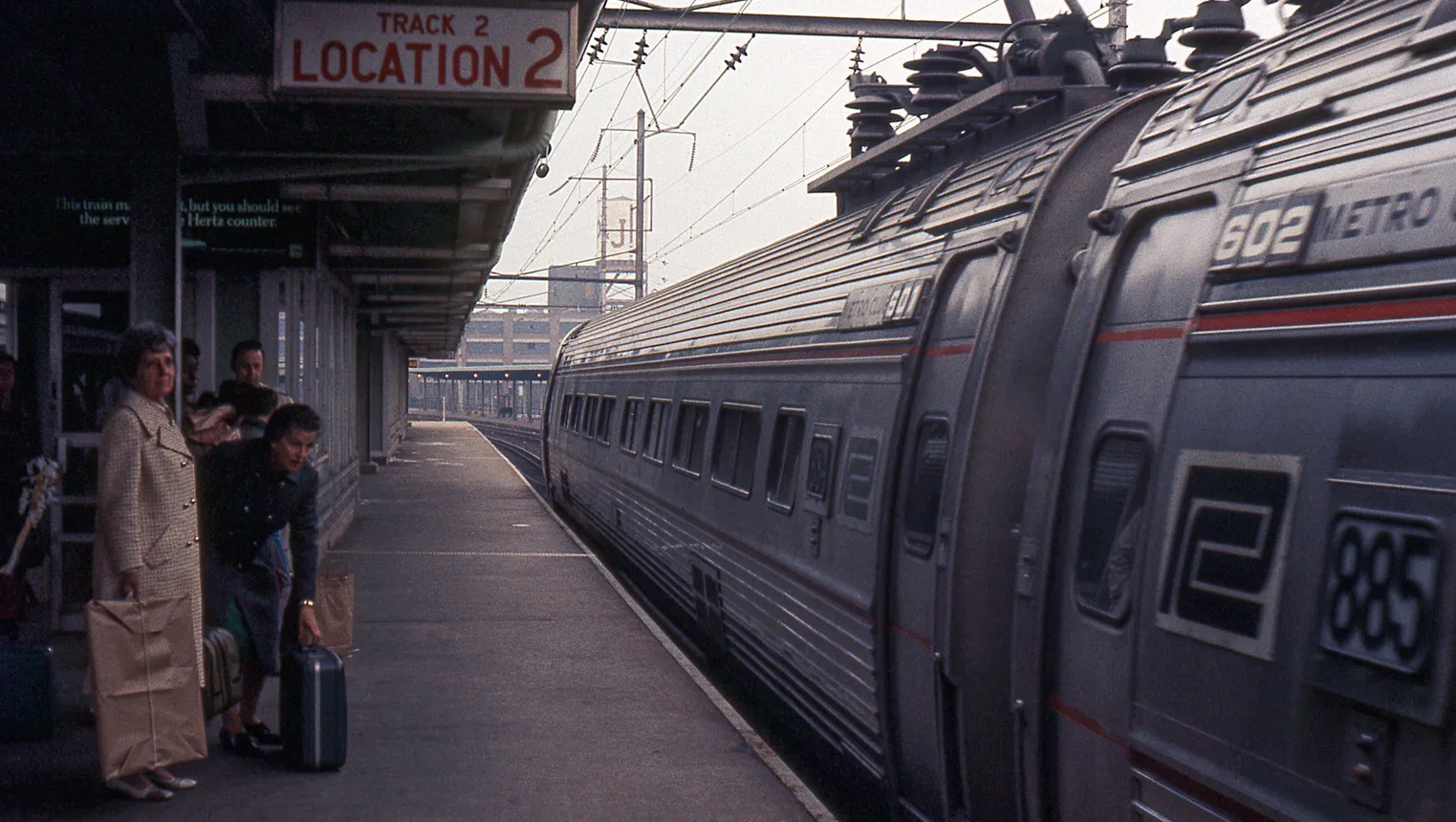 Train station platform with several people and part of a passenger train arriving.