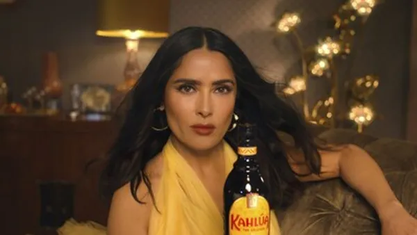 Salma Hayek holds a bottle of Kahlúa while wearing a yellow dress.
