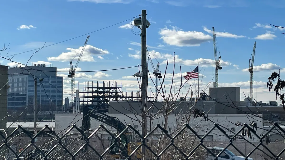 Fence in the foreground, construction cranes in the background