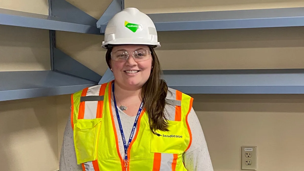 A woman with a hardhat stands in front of a construction site