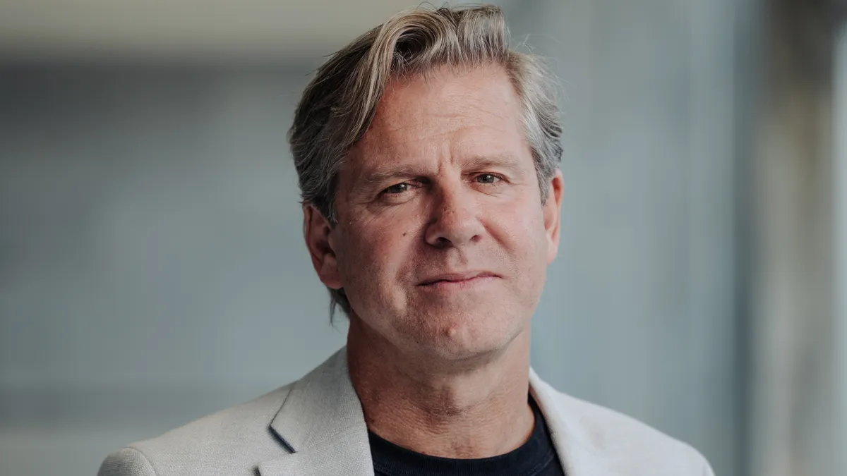 A man in a black T-shirt and beige blazer