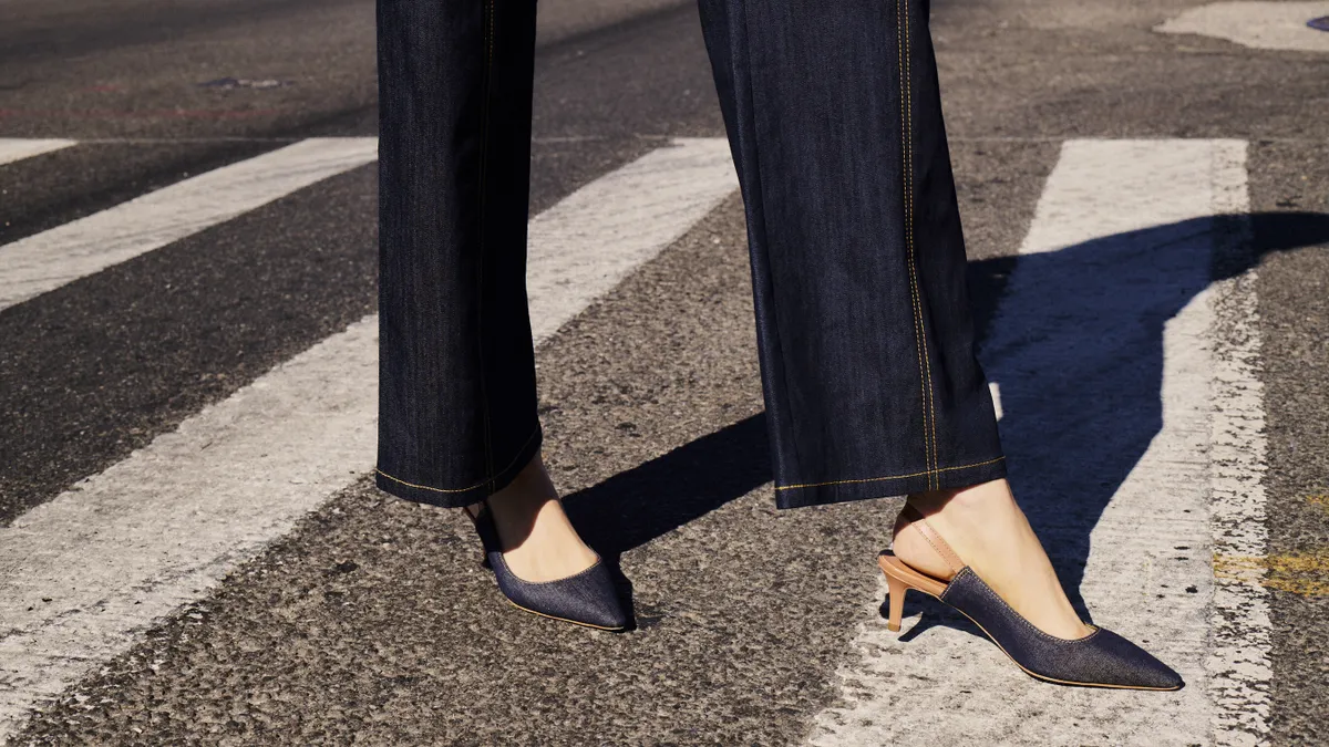 A person in jeans wears a pair of denim shoes and stands on a street.