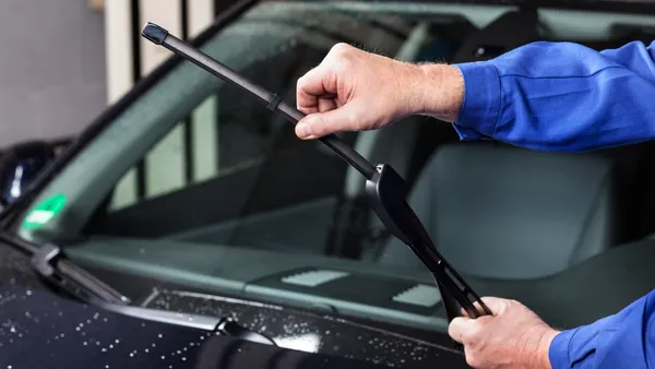A hand pulls up a windshield wiper on a car to check it