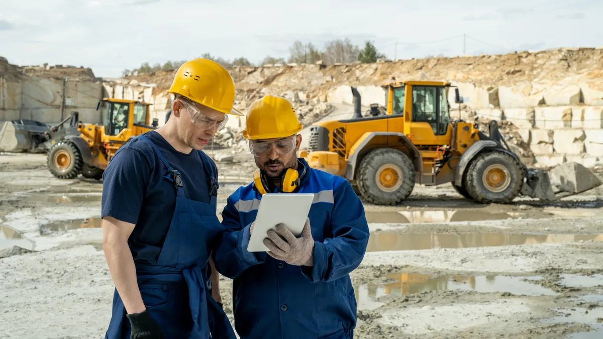 Two builders in workwear looking at sketch of building on tablet screen