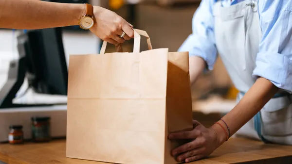 a worker hands over a paper bag to a customer's hand