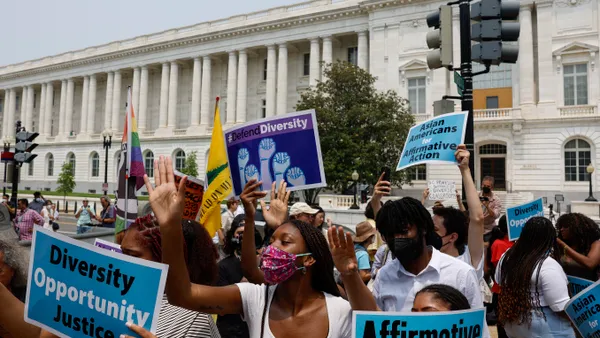 A group of people in masks stand outside a government building, holding signs in support of affirmative action.