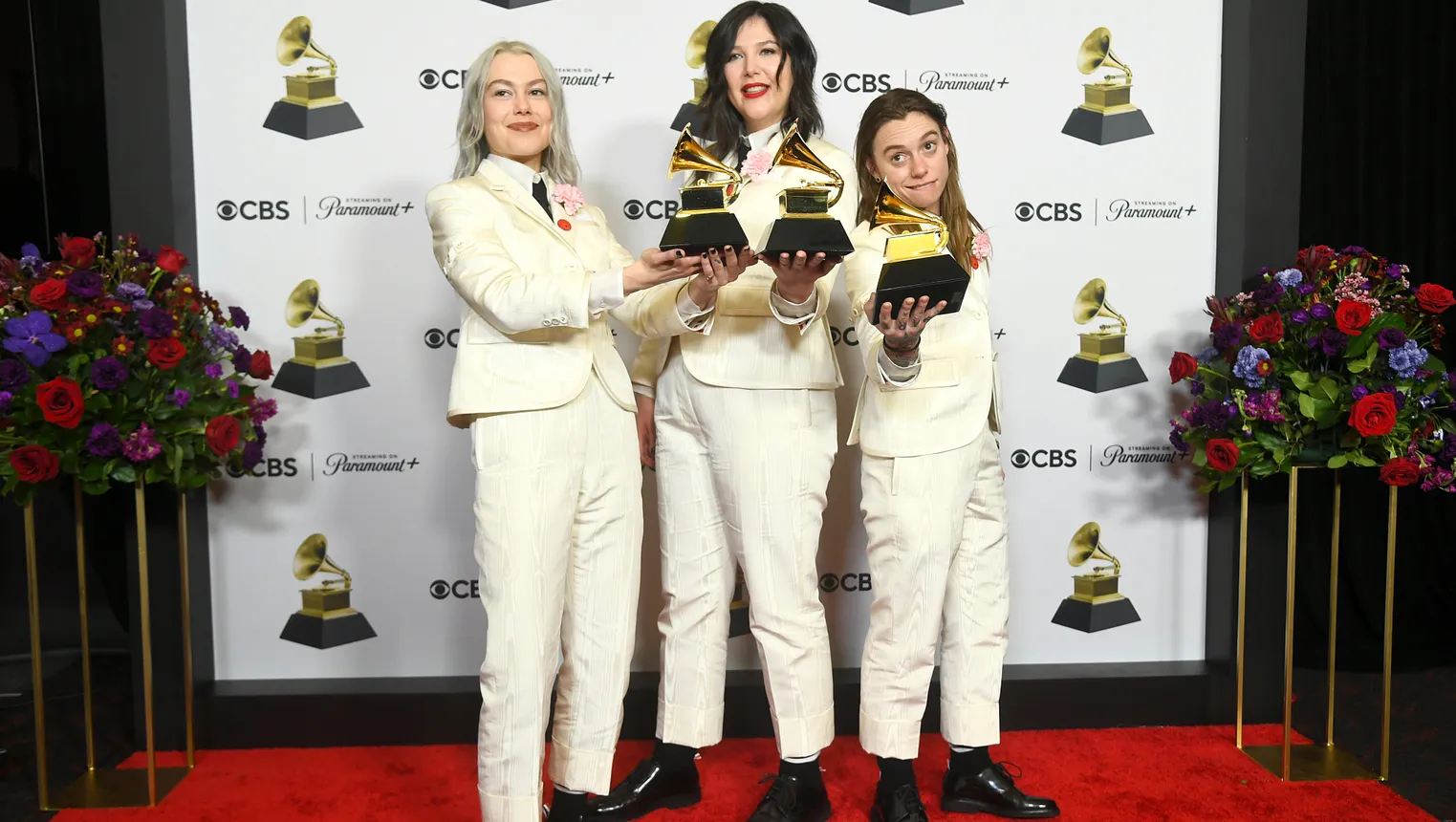 Boygenius members Phoebe Bridgers, Lucy Dacus and Julien Baker holds Grammy awards and wear matching white suits.