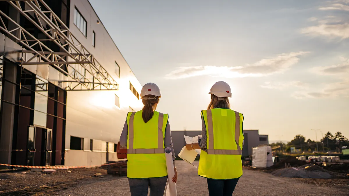 Two women on a jobsite wearing protective gear and holding documents.