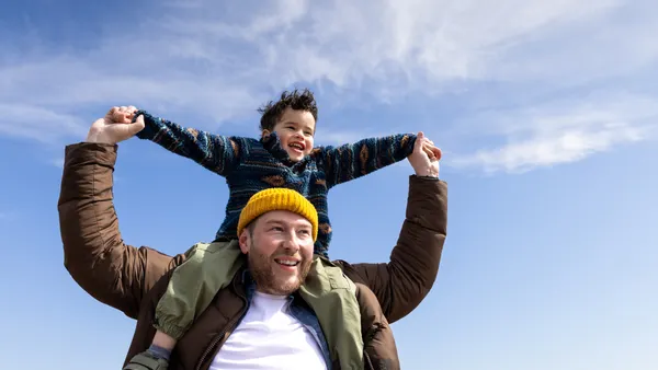 A waist-up shot of a young boy on top of his father's shoulders walking along Alnmouth Beach, Northumberland.