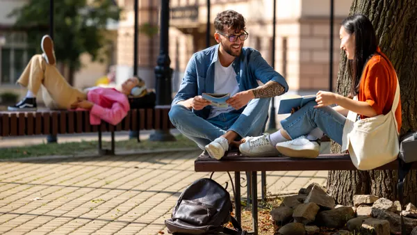 Two college students sit on a bench and talk.