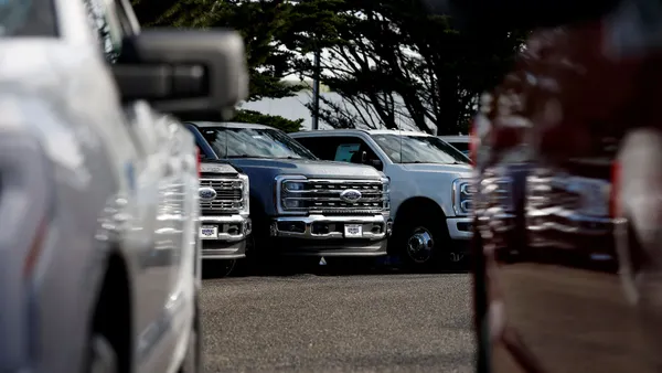 Two vehicles are parked side by side while a lineup of Ford trucks is parked in the background.