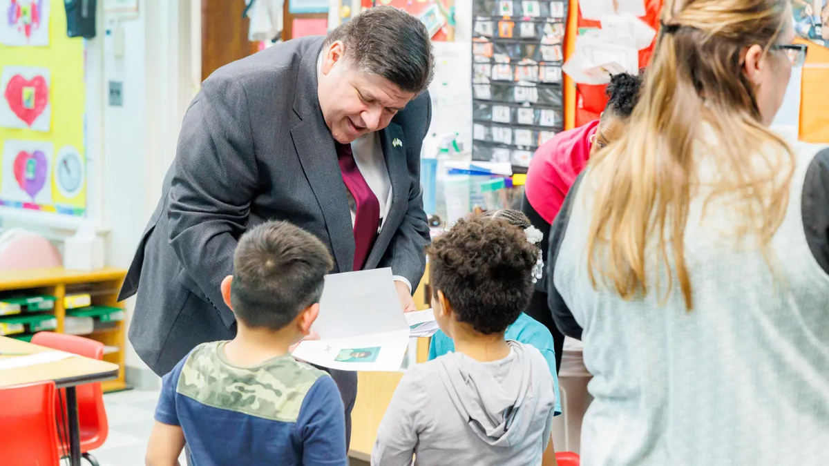 Illinois Governor J.B. Pritzker bends down and smiles at a young student