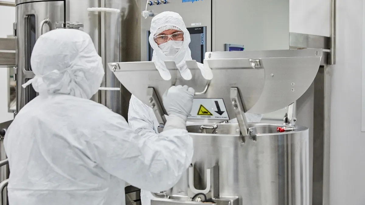 Two personnel in a manufacturing room wearing protective gear.