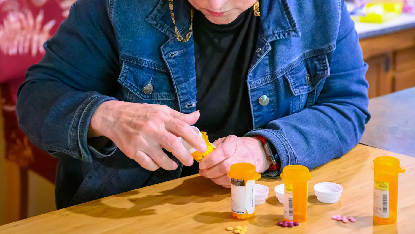 A person sits at a table and pours pills into there hand.