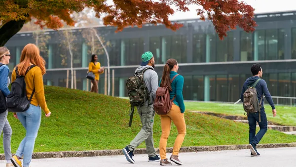 Group of students walking and standing in front of a modern glass university building