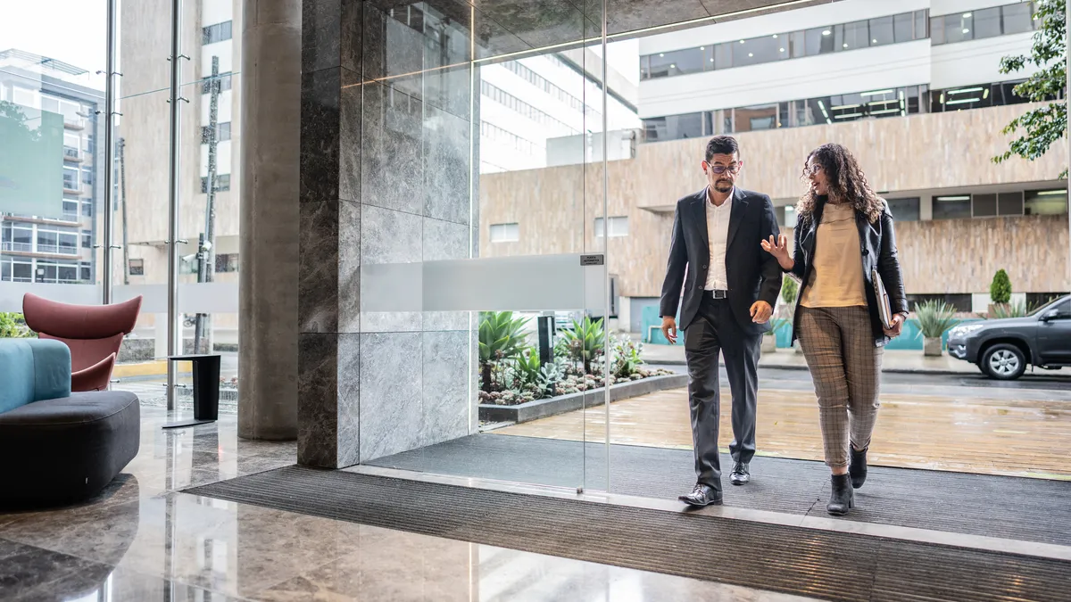 Two coworkers walk into a modern office building.