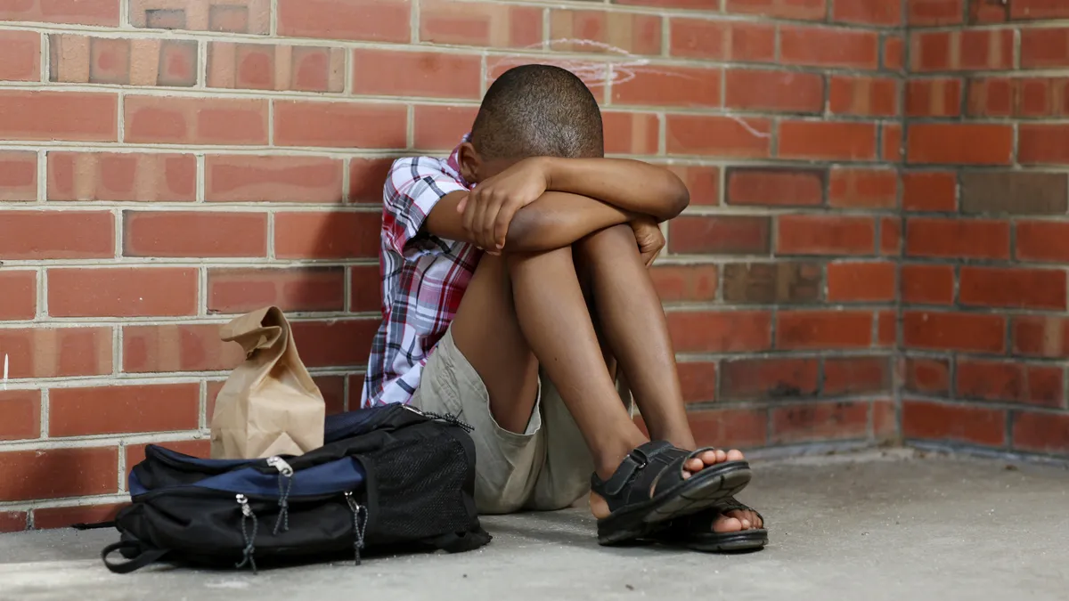 Young boy sitting alone with head buried against a brick wall