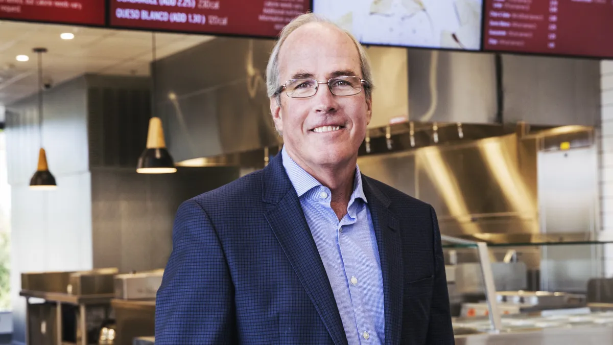 An image of a man wearing a suit in front of a Chipotle menu and make line.